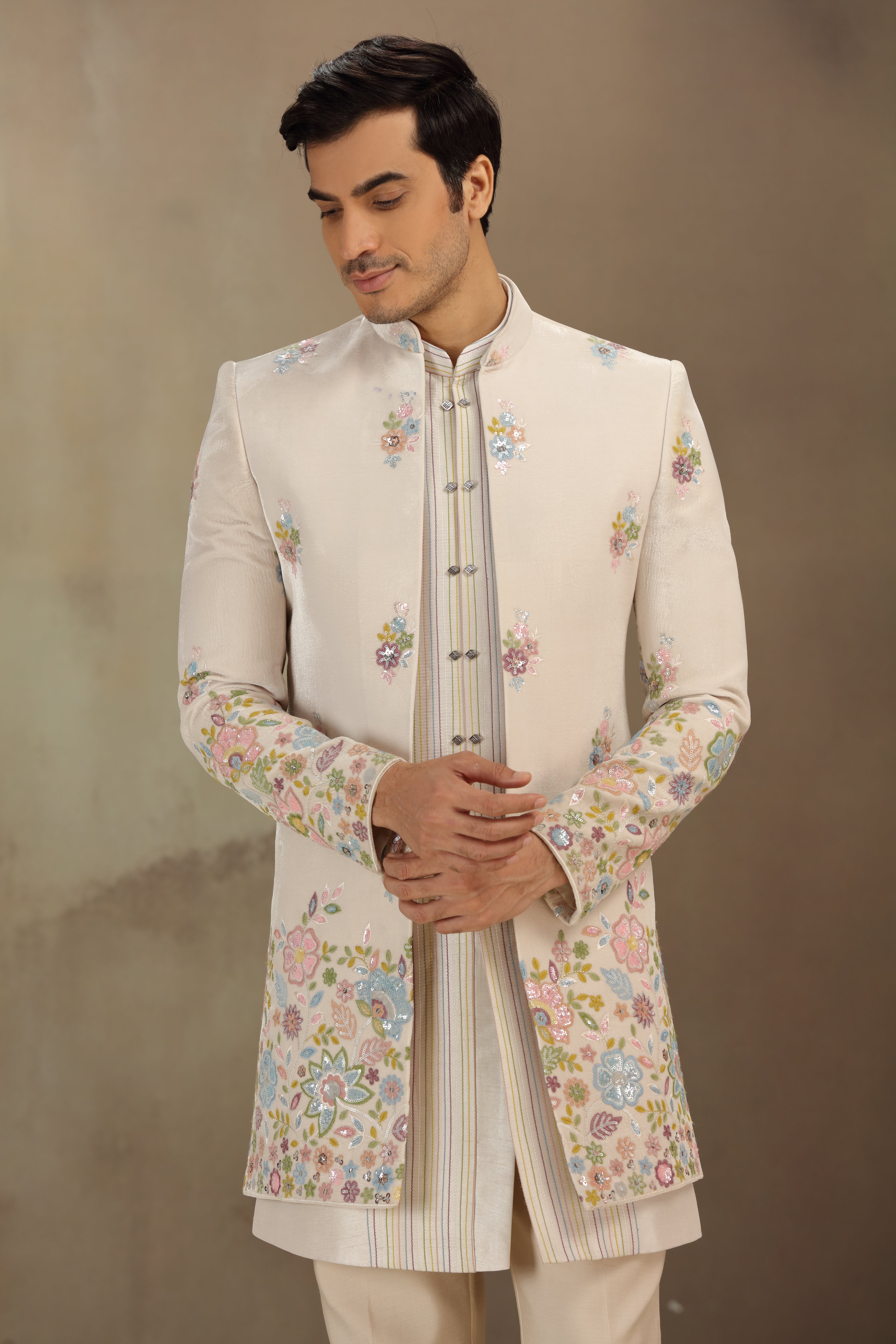 Man wearing a traditional embroidered sherwani against a plain background